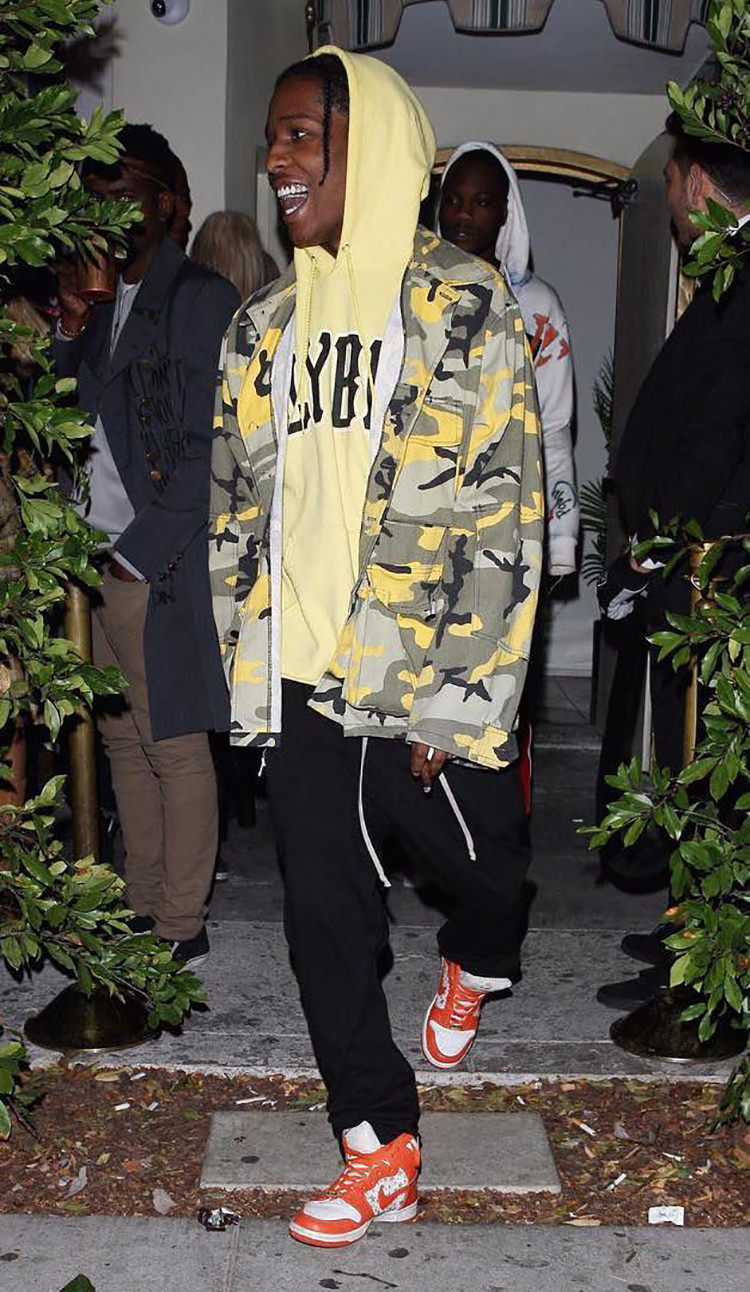 ASAP Rocky pairs the Supreme x Nike SB Dunk High with loose sweats, a graphic hoodie, and a camo jacket.
